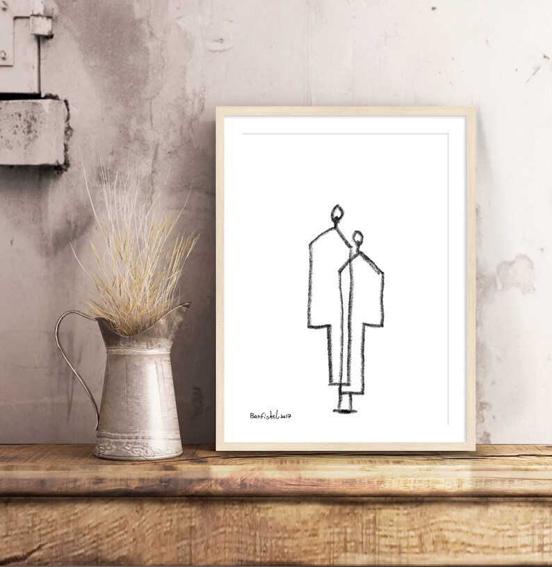 May include: Black and white line drawing of two figures standing side by side. The drawing is framed in a light wood frame and is on a wooden surface.