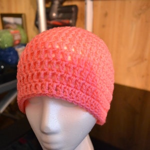 Puede incluir: Un gorro tejido a ganchillo de color coral. El gorro se exhibe en una cabeza de maniqu&iacute;, mostrando su dise&ntilde;o de tejido abierto. El color del gorro es un tono vibrante y c&aacute;lido, perfecto para a&ntilde;adir un toque de color a cualquier atuendo.