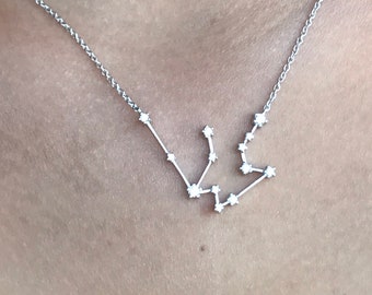 May include: A silver chain necklace with a constellation pendant featuring small, clear stones. The constellation is shaped like the astrological sign Aquarius.