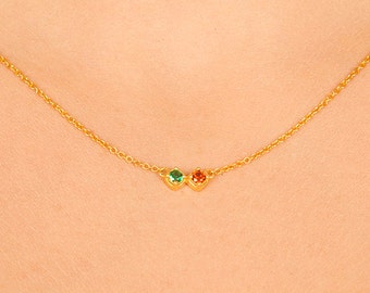 Puede incluir: Un collar de cadena de oro con una pequeña piedra preciosa verde y una pequeña piedra preciosa roja.