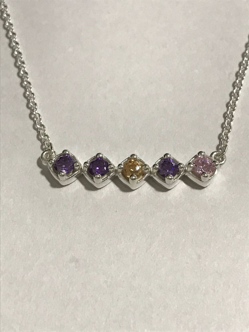 Puede incluir: Un collar de cadena de plata con cinco piedras preciosas. Las piedras preciosas son moradas, moradas, doradas, moradas y rosadas.