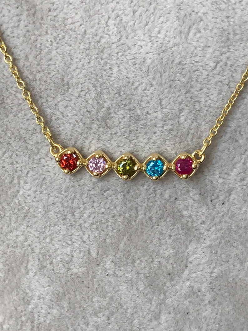 Puede incluir: Un collar de cadena de oro con un arco&iacute;ris de piedras preciosas. Las piedras est&aacute;n dispuestas en fila y son rojas, rosas, verdes, azules y rojas.