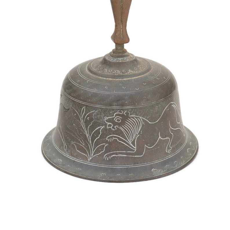 Op de afbeelding: Een bronzen bel met een houten handvat, versierd met een gegraveerd ontwerp van een leeuw en bladeren.
