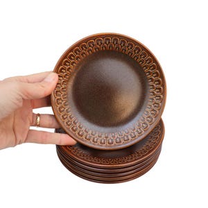 May include: A stack of brown ceramic plates with a decorative pattern. The plates are all the same size and have a slightly textured surface.