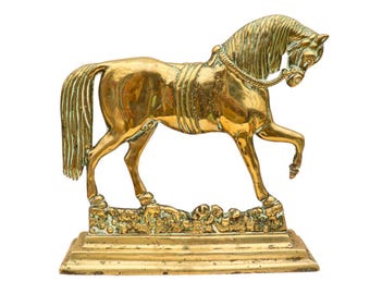May include: A gold-colored brass horse doorstop with a detailed design. The horse is standing on a base with a textured surface.