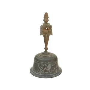 Op de afbeelding: Een bronzen bel met een decoratief handvat met een staand figuur. De bel heeft een ronde basis met een gegraveerd ontwerp van een leeuw en bladeren.