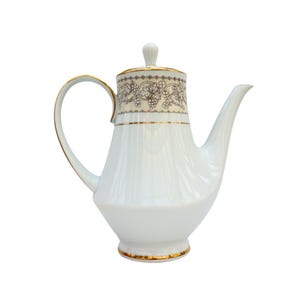 May include: White porcelain teapot with a gold trim and a floral design. The teapot has a lid and a spout.