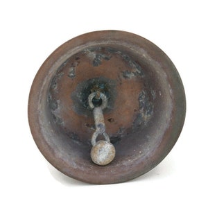 Op de afbeelding: Een vintage, koperkleurige bel met een versleten, verweerde afwerking. De bel heeft een metalen lus en een kleine, ronde knop aan het einde van de lus.