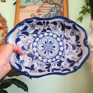 May include: A decorative ceramic serving dish with a scalloped edge. The dish features a white base with a blue floral design and a central flower motif. The rim and edge are painted in a deep blue color.