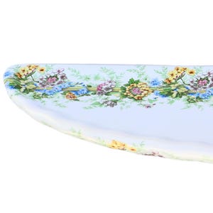 May include: A white oval serving platter with a floral border design. The border features blue, yellow, and pink flowers with green leaves.