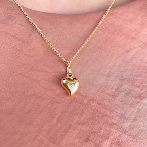 May include: A gold chain necklace with a small, heart-shaped pendant.
