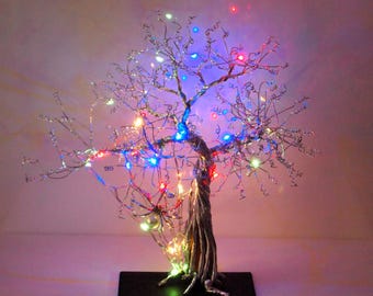 May include: A silver wire tree sculpture with colorful LED lights. The lights are red, blue, green, and white. The tree is on a black base.