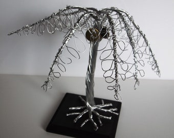 May include: A silver wire sculpture of a palm tree with a black base. The tree has a twisted trunk and a full canopy of leaves.