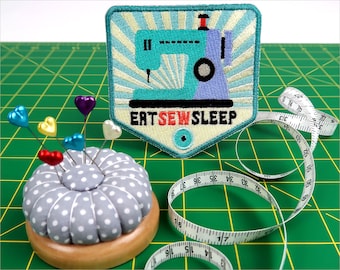 Puede incluir: Un parche de máquina de coser colorido con el texto "Eat Sew Sleep" en una alfombra de corte verde con un cojín de alfileres y una cinta métrica.