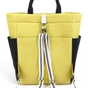 May include: A yellow tote bag with black accents and a white and black patterned strap. The bag has a top handle and adjustable straps that can be worn as a backpack.