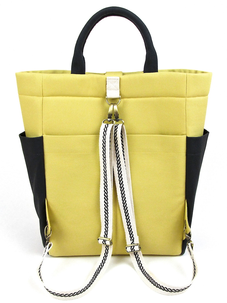 May include: A yellow tote bag with black accents and a white and black patterned strap. The bag has a top handle and adjustable straps that can be worn as a backpack.