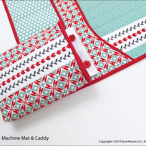 May include: A red and green fabric machine mat and caddy with a floral pattern and black stitching. The caddy is folded and the mat is visible in the background.