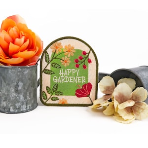 Peut inclure: Un patch brodé vert et blanc avec le texte "Happy Gardener" entouré de fleurs et de baies colorées.