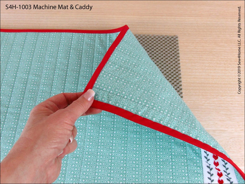 May include: A turquoise blue machine quilting mat with a red binding and a white and green heart pattern. The mat is folded over a gray non-slip mat.