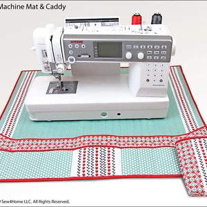 May include: A white sewing machine with a teal and red patterned mat and a matching caddy. The mat has pockets for storing sewing supplies. The machine has a digital display and a variety of buttons. The text "JANOME" is visible on the machine.