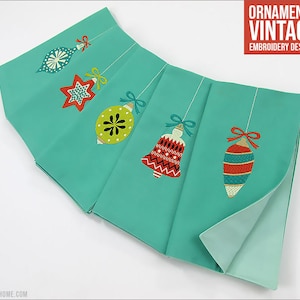 May include: Five teal fabric squares with embroidered vintage Christmas ornaments. The ornaments include a star, a bell, and three different shaped bulbs. The text "ORNAMENTS VINTAGE EMBROIDERY DESIGNS" is at the top of the image.