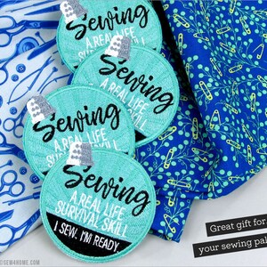 Puede incluir: Cuatro parches redondos bordados de color azul turquesa con el texto "Coser Una habilidad de supervivencia de la vida real" y "Yo coso. Estoy listo." Los parches est&aacute;n sobre una tela azul con un patr&oacute;n de imperdibles.