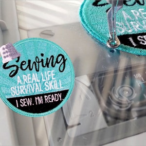 Puede incluir: Un parche redondo de color azul turquesa con bordado blanco y negro. El texto en el parche dice "Sewing A Real Life Survival Skill I Sew. I'm Ready."