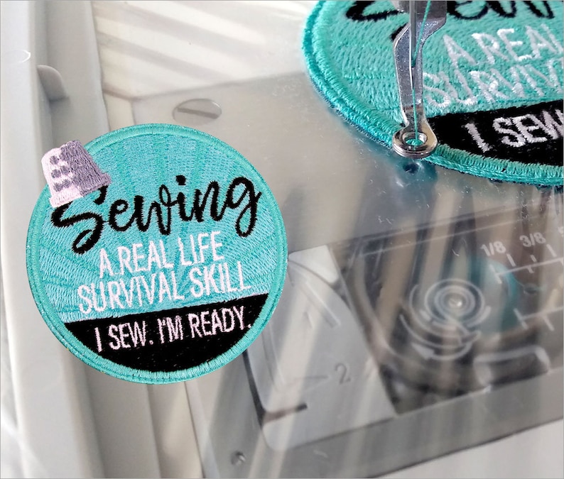 Puede incluir: Un parche redondo de color azul turquesa con bordado blanco y negro. El texto en el parche dice "Sewing A Real Life Survival Skill I Sew. I'm Ready."