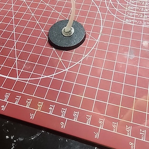 A single curved clear plastic flight stand mounted upright on a round black base sitting on a red hobby cutting mat.