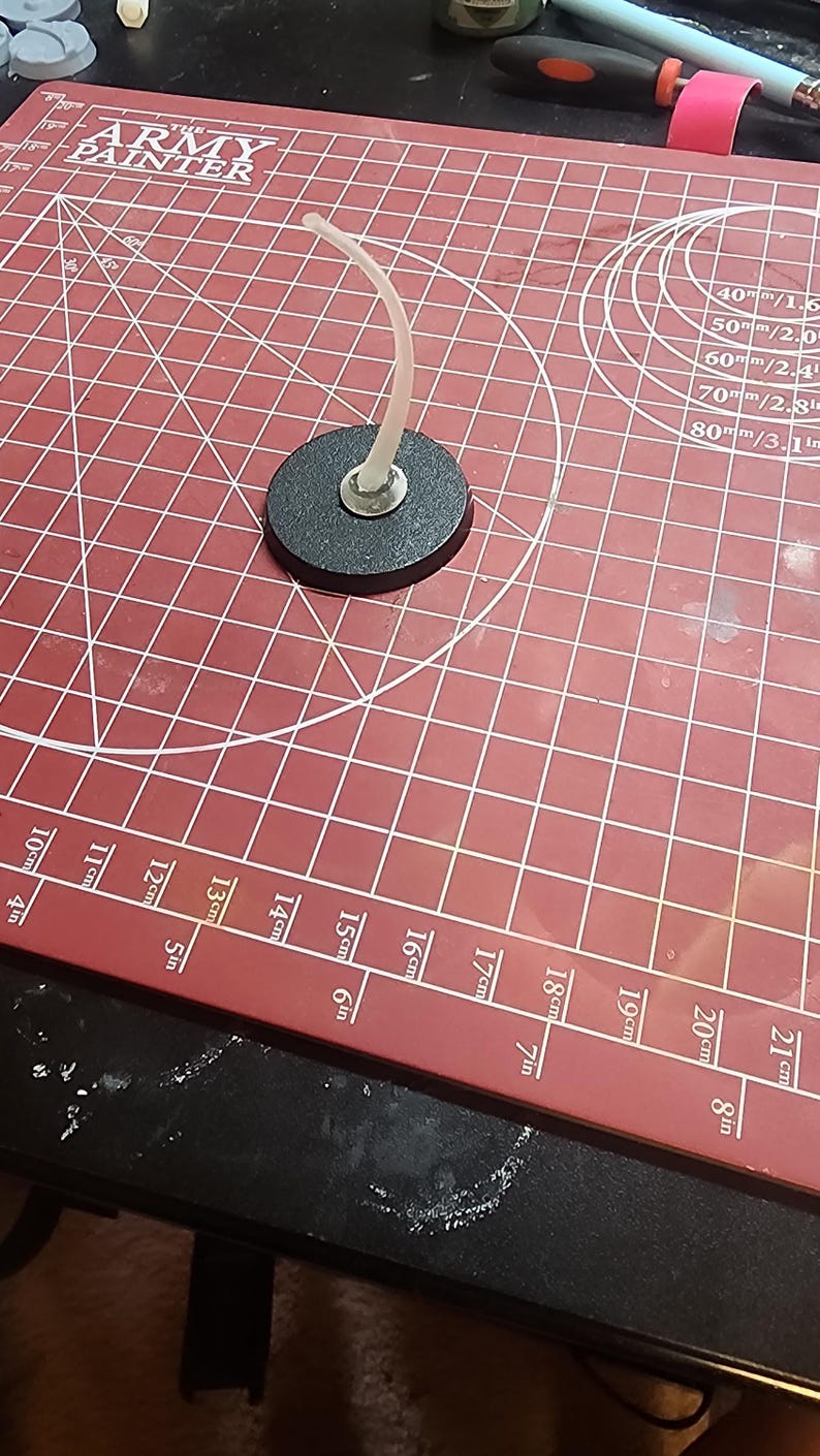 A single curved clear plastic flight stand mounted upright on a round black base sitting on a red hobby cutting mat.