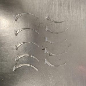 May include: A set of ten clear plastic tubing with a curved shape. The tubing is arranged in rows on a silver surface.
