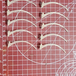 Ten curved clear plastic flight stands laid out in two parallel rows on a red cutting mat with white grid lines.