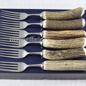May include: Set of six stainless steel forks with stag horn handles in a blue box. The forks are arranged in a row with the handles facing up.