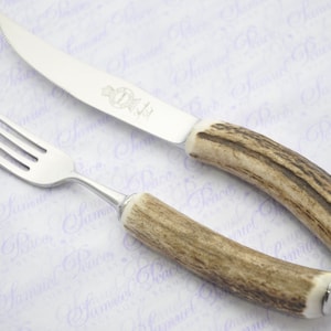 Puede incluir: Un juego de dos cubiertos de plata con mangos de asta de ciervo. El cuchillo tiene una hoja de plata y el tenedor tiene cuatro dientes.