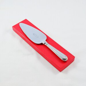 May include: A silver cake server with an ornate handle is presented in a red box.