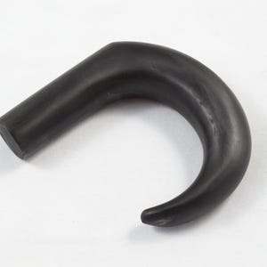 Pode incluir: Uma pega de madeira preta curva, possivelmente para uma bengala ou bengala, é exibida contra um fundo branco. A pega tem uma aparência lisa e polida e um design arredondado e ergonómico. A pega tem cerca de 15 cm de comprimento.