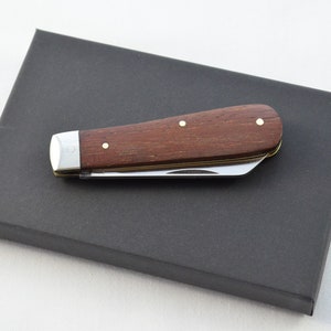 以下が含まれることがあります： 木製のハンドルとステンレス製のブレードを持つポケットナイフ。ハンドルには真鍮のリベットが3つ付いています。