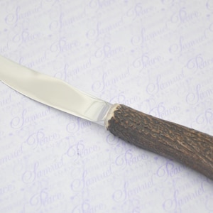 May include: A silver knife with a brown antler handle. The handle has a silver cap on the end.