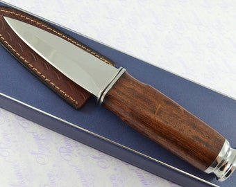 May include: A silver knife with a brown wooden handle and a leather sheath. The knife is in a blue box with a white background.