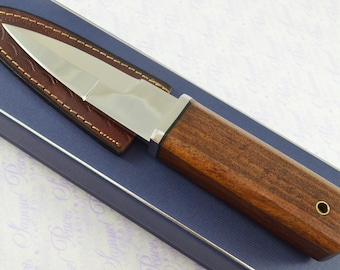 May include: A small, silver knife with a wooden handle. The knife is in a brown leather sheath and is sitting on a blue box.
