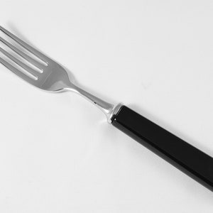 May include: A stainless steel fork with a black handle. The fork has four tines and a polished finish. The handle is rectangular and smooth. The fork is designed for eating and is suitable for everyday use.