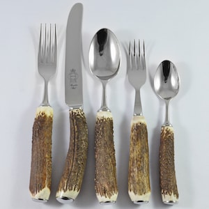 May include: Set of five silver cutlery pieces with antler handles. The set includes a knife, two forks, and two spoons.