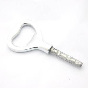 Può includere: Un apribottiglie argentato con un'apertura a forma di cuore e un manico lungo e sottile.