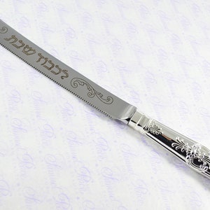 May include: Silver cake knife with an ornate handle and a serrated blade. The blade is engraved with the Hebrew words "Mazel Tov" which means "Congratulations".