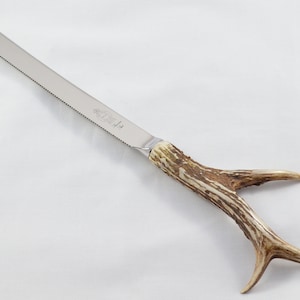 May include: A silver bread knife with a serrated edge and a brown antler handle.