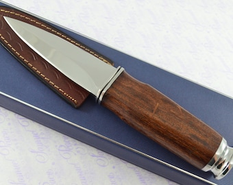 May include: A silver knife with a brown wooden handle and a leather sheath. The knife is in a blue box with a white background.
