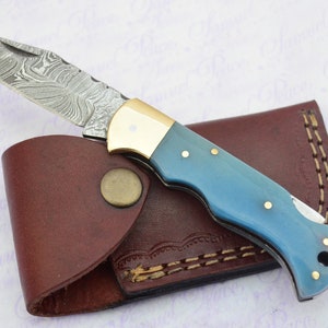 May include: A small pocket knife with a blue handle and a damascus steel blade. The knife is in a brown leather sheath.