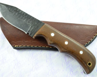 May include: A brown handled knife with a black blade and a leather sheath. The blade has a hammered finish.