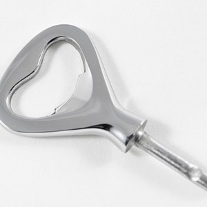 May include: A silver bottle opener with a heart-shaped opening. The opener has a long, thin handle.