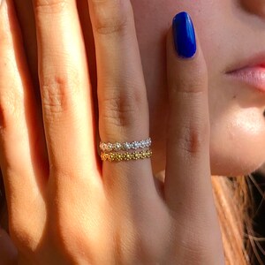 Könnte beinhalten: Zwei zarte Ringe an einem Finger. Der obere Ring ist silber und der untere Ring ist gold. Beide Ringe bestehen aus kleinen, runden Perlen.